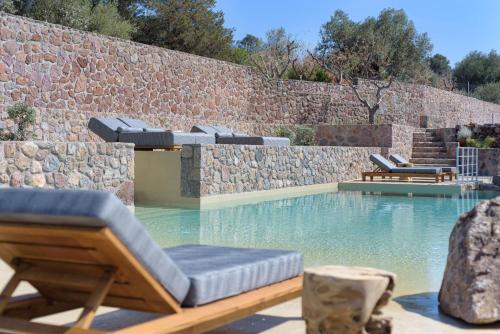 a swimming pool with chairs and a stone wall at Aelia & Melitta Villas in Perdika