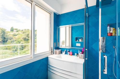 une salle de bains bleue avec lavabo et fenêtre. dans l'établissement VILLA NICE-GAIRAUT by RIVIERA HOLIDAY HOMES, à Nice