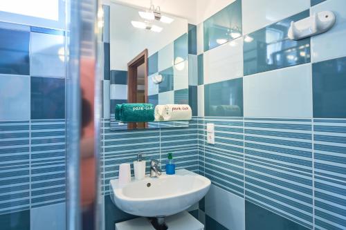 a blue tiled bathroom with a sink and a mirror at Park-Lak Vendégház in Makó