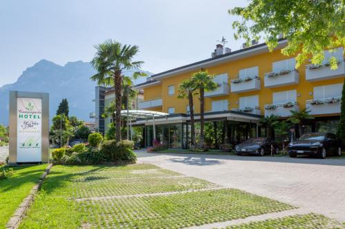 a large yellow building with palm trees and a street at Hotel Campagnola in Riva del Garda