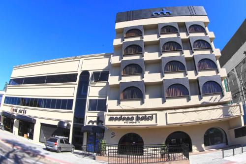 a white building with a car parked in front of it at Hotel Modena - São José dos Campos in São José dos Campos