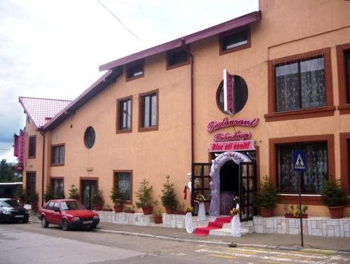 une voiture rouge garée devant un bâtiment dans l'établissement Pensiune Restaurant Brândușa, à Suceava