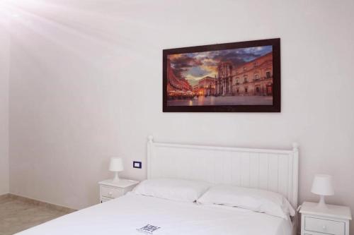 une chambre avec un lit blanc avec un tableau sur le mur dans l'établissement Paolanna Rooms Affittacamere, à Syracuse