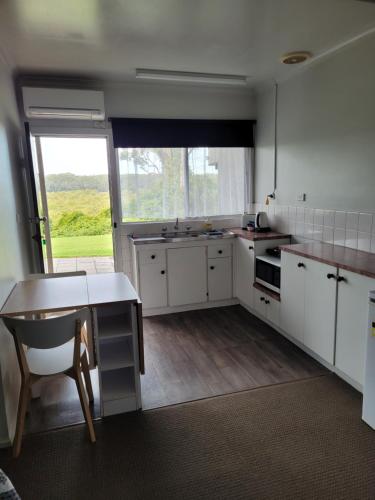 een keuken met witte kasten en een tafel en een raam bij Jabiru Motel in Nambucca Heads