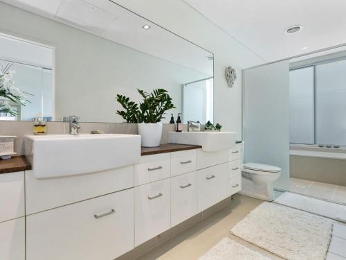 a white bathroom with two sinks and a toilet at COASTAL CHIC @ CASUARINA in Casuarina