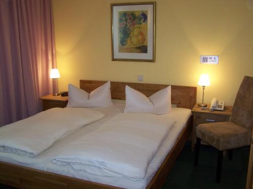 a bedroom with a bed with white sheets and a chair at Hotel Am Stiftsberg in Aschaffenburg