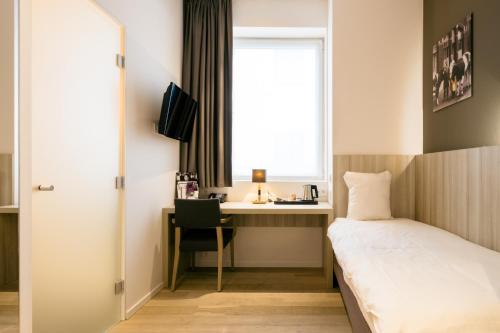 a bedroom with a bed and a desk and a window at C-Hotels Westwing - ex Mercure in Roeselare