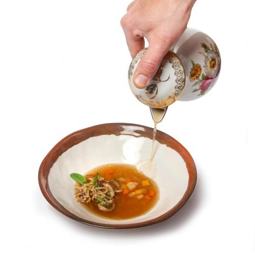 a person pouring soup from a tea cup into a bowl at Hiša Linhart, Hotel & Restaurant in Radovljica