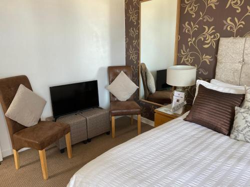 a bedroom with a bed and two chairs and a tv at Beechwood Ensuite Guest House in Ayr