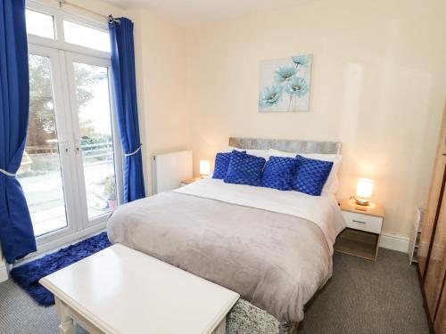 a bedroom with a bed with blue pillows and a window at Llys Madoc, Basement Apartment in Penmaen-mawr