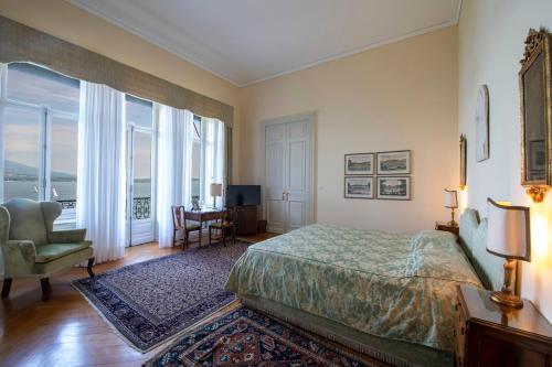 a bedroom with a bed and a chair and windows at Villa Claudia dei Marchesi Dal Pozzo in Belgirate