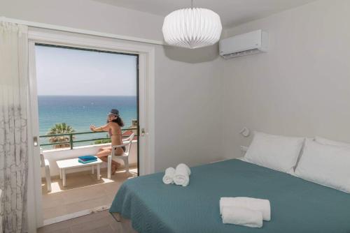 Aria, Maisonette in Glyfada Beach في غليفادا: امرأة تجلس على كرسي على شرفة مع المحيط