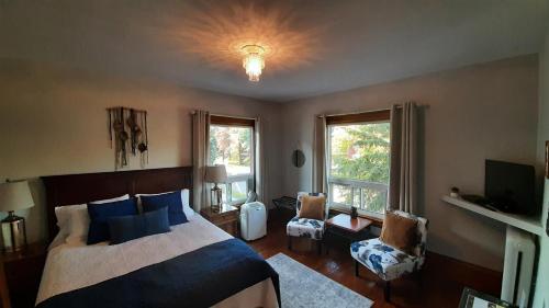 a bedroom with a bed and a tv and two windows at Stonewater Manor B&B in Gananoque
