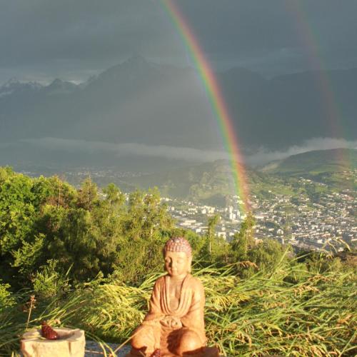 a statue of a monk sitting on a hill with a rainbow at Domaine Bellevie BnB in Vex
