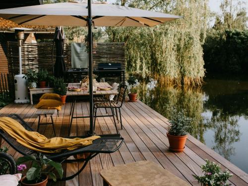 una terraza de madera con sombrilla, mesa y sillas en Chalet in Geel in quiet location by the water, en Geel