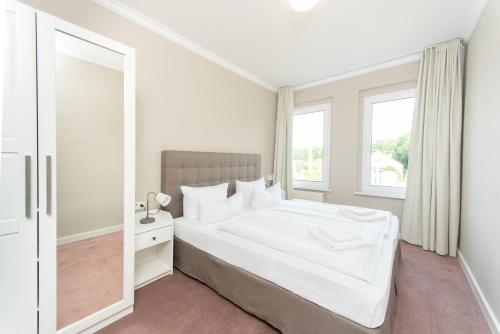 a white bedroom with a large bed and a mirror at Appartementhaus Zum Strandkorb in Kühlungsborn