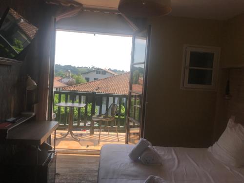 a bedroom with a bed and a balcony with a table at Hotel Mendionde in Saint-Pée-sur-Nivelle