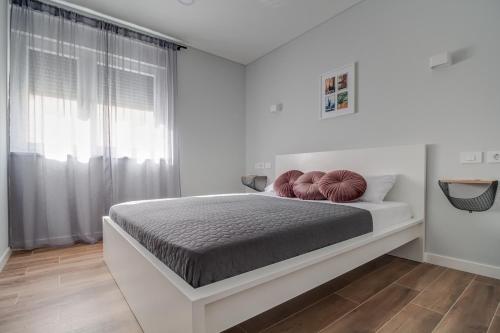 ein weißes Schlafzimmer mit einem Bett mit zwei roten Kissen darauf in der Unterkunft B & R Summer breeze apartments in Nin