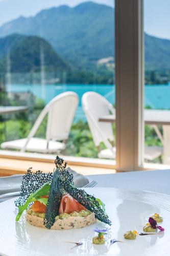 a plate of food on a table with a view of the ocean at Hôtel Beau Site Talloires B SPA in Talloires