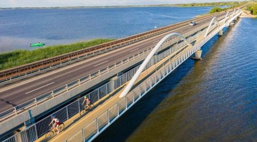 two people riding bikes on a bridge over the water at Thermál Apartman Tiszafüred in Tiszafüred