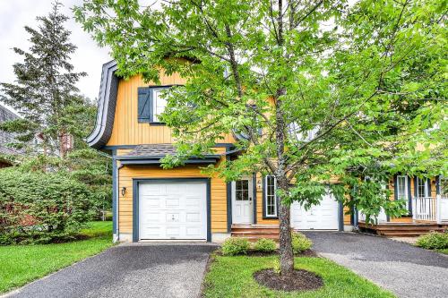 a yellow house with two garage doors and a tree at Townhouse With Free Shuttle To Tremblant Resort in Mont-Tremblant