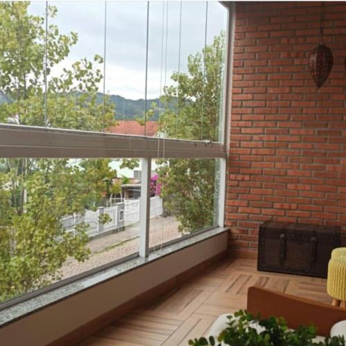 a room with a large window and a brick wall at Melhor Apartamento centro Pomerode, perto de tudo in Pomerode
