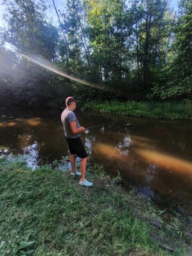a man standing in a river holding a fishing rod at Mazā Kāpa in Koknese