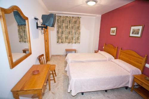 a room with two beds and a table and a mirror at Hostal Miguel y Juani in L'Alcúdia