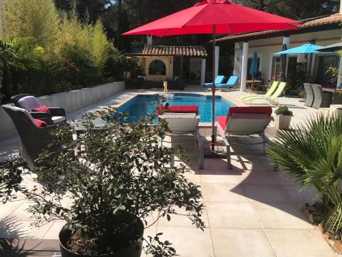 - une piscine avec des chaises et un parasol rouge dans l'établissement VILLA NATURISTE JO&SPA ANNA'BELLA Luxury Suites "naturist couples only", au Cap d'Agde