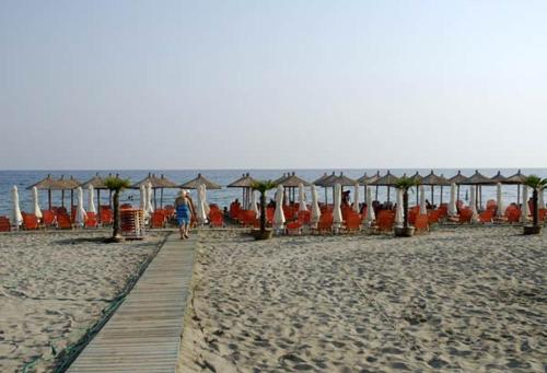 a person walking on a beach with chairs and umbrellas at Olympic Beach Hotel in Nei Poroi