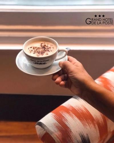 a person holding a cup of coffee on aucer at Grand Hôtel de la Poste in Saint-Jean-de-Luz