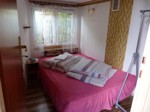 a bedroom with a bed with pink sheets and a window at Domek + pokoje nad kanałem in Augustów