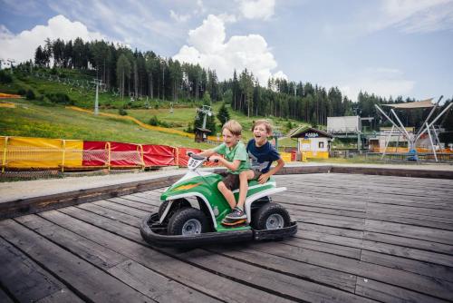 two children riding a toy scooter on a boardwalk at APARTMENT WALD - im Skigebiet Gerlitzen & Ossiacher See in Bodensdorf
