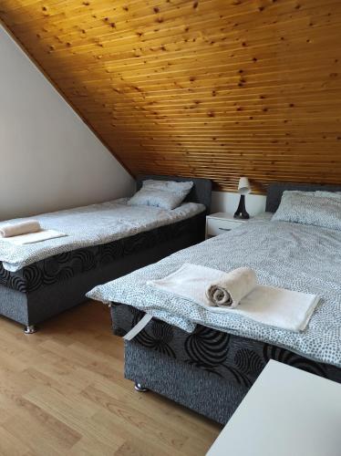 two beds in a room with a wooden ceiling at Kamilla Vendégház Tiszafüred in Tiszafüred