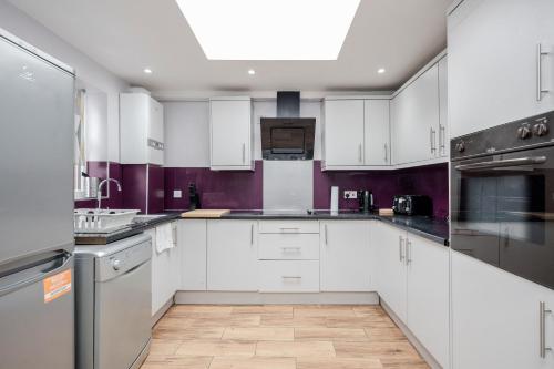 a kitchen with white cabinets and purple walls at Everything You Need I Super Comfy I Sleeps 7 I WiFi I Parking I 4BDR in Dagenham
