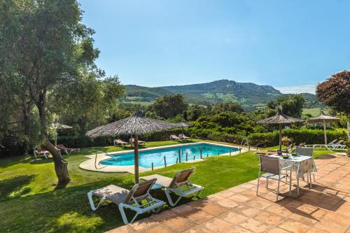 a swimming pool with two lawn chairs and an umbrella at Hotel-Apart CORTIJO LAS PIÑAS in Tarifa