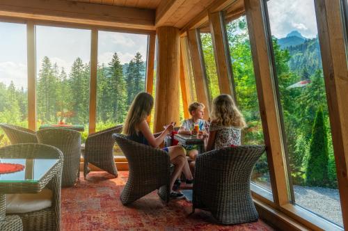 three girls sitting at a table in a room with windows at Hotel Eco Tatry Holiday& Spa in Kościelisko