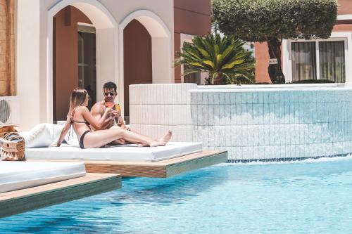 a group of people sitting on beds next to a swimming pool at Zeus Village Resort - Adults Only in Kato Daratso