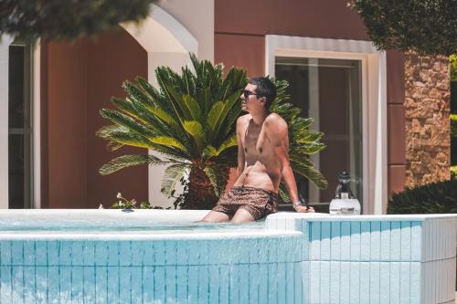 a man in a bathing suit sitting in a swimming pool at Zeus Village Resort - Adults Only in Kato Daratso