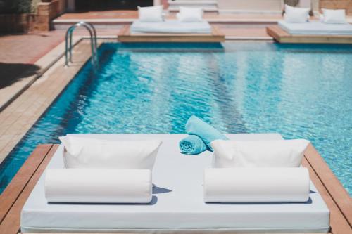 a pool with white chaise lounge chairs next to a swimming pool at Zeus Village Resort - Adults Only in Kato Daratso