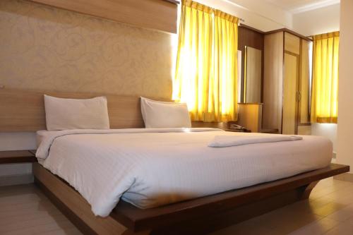 a bedroom with a large white bed with yellow curtains at HOTEL SRI VAARI RESIDENCY in Hosūr