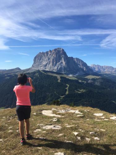 a woman taking a picture of a mountain at Arya Alpine Lodge in Selva di Val Gardena