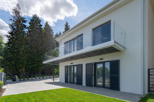 a white house with black shutters and a lawn at Rózsabors Hévíz in Hévíz
