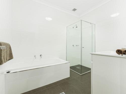 La salle de bains blanche est pourvue d'un lavabo et d'une douche. dans l'établissement Surf Beach Dreams, à Kiama