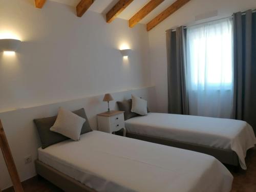 two beds in a hotel room with a window at Ares do Monte - Turismo Rural in Cercal