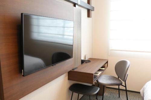 a tv hanging on a wall with a desk and two chairs at Hotel The M's Kyoto in Kyoto