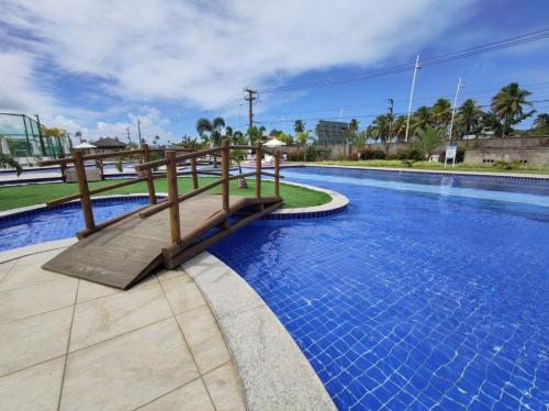 a swimming pool with a wooden bridge and blue water at Porto de Galinhas | Muro Alto 116B in Porto De Galinhas