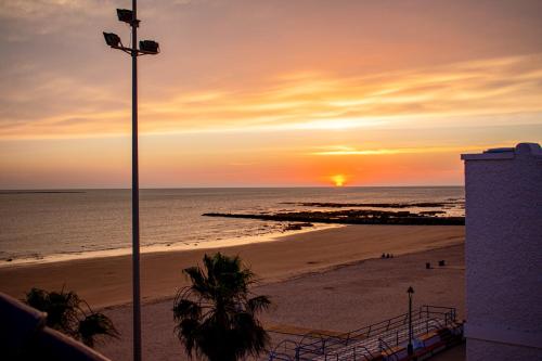 a sunset on the beach with a light pole at Hotel Playa de Regla in Chipiona