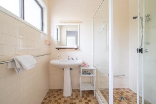 La salle de bains blanche est pourvue d'un lavabo et d'une douche. dans l'établissement Beach Shack semi detached, 2 Min Walk to Beach - Wattle, à Pearl Beach