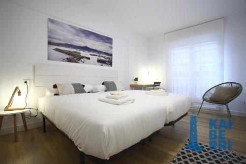 a white bedroom with a large bed and a chair at Guadalupenea by Kaiberri Inmo in Hondarribia